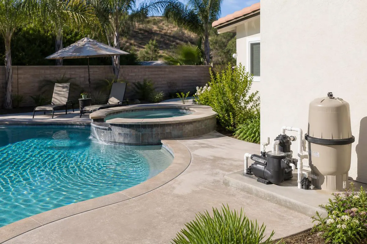 A backyard swimming pool and raised spa with the pool equipment pad beside the house