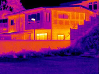 Infrared image of a house at night, its warm windows and walls in orange against a cool purple sky